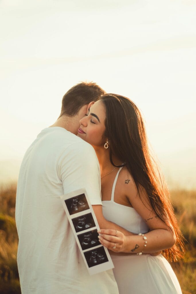 Happy Couple Hugging While Woman Holding Ultrasound Pictures of Baby