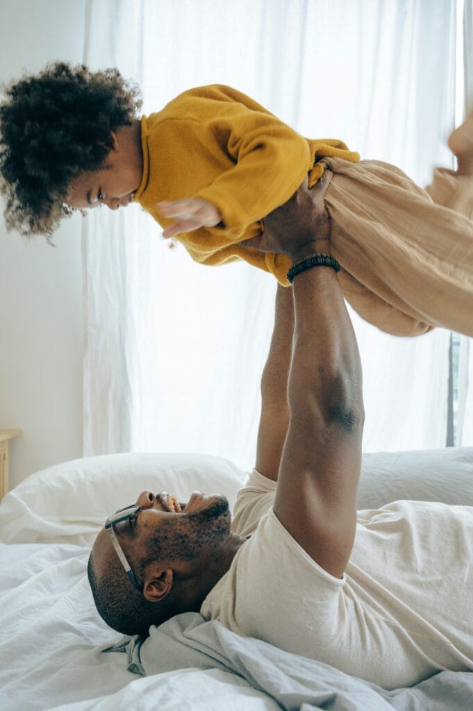 A joyful moment at home with a father lifting his son in a cozy bedroom.
